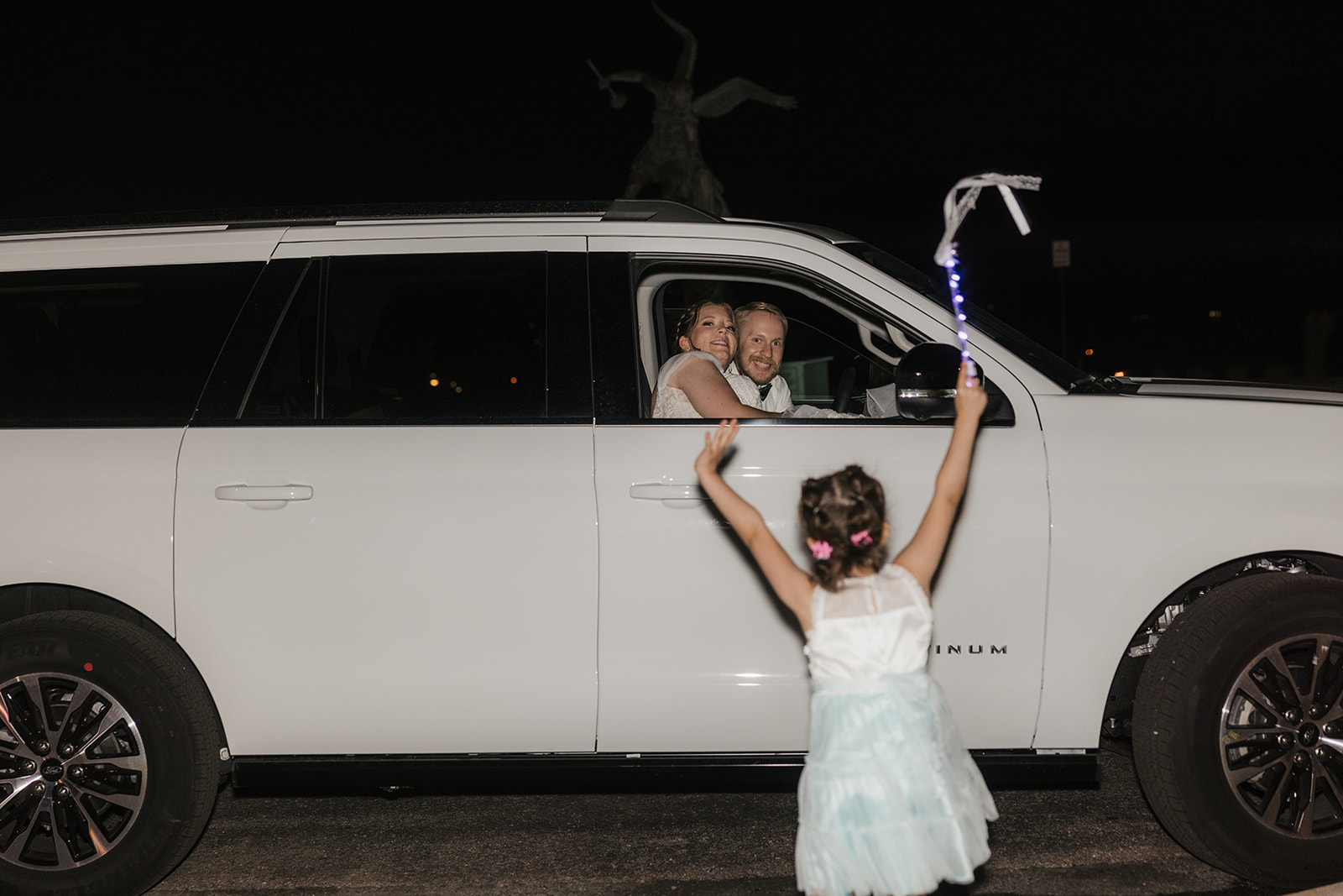 catholic wedding photos of A bride and groom walk outside at night as guests hold up lights and ribbons, celebrating their wedding.
