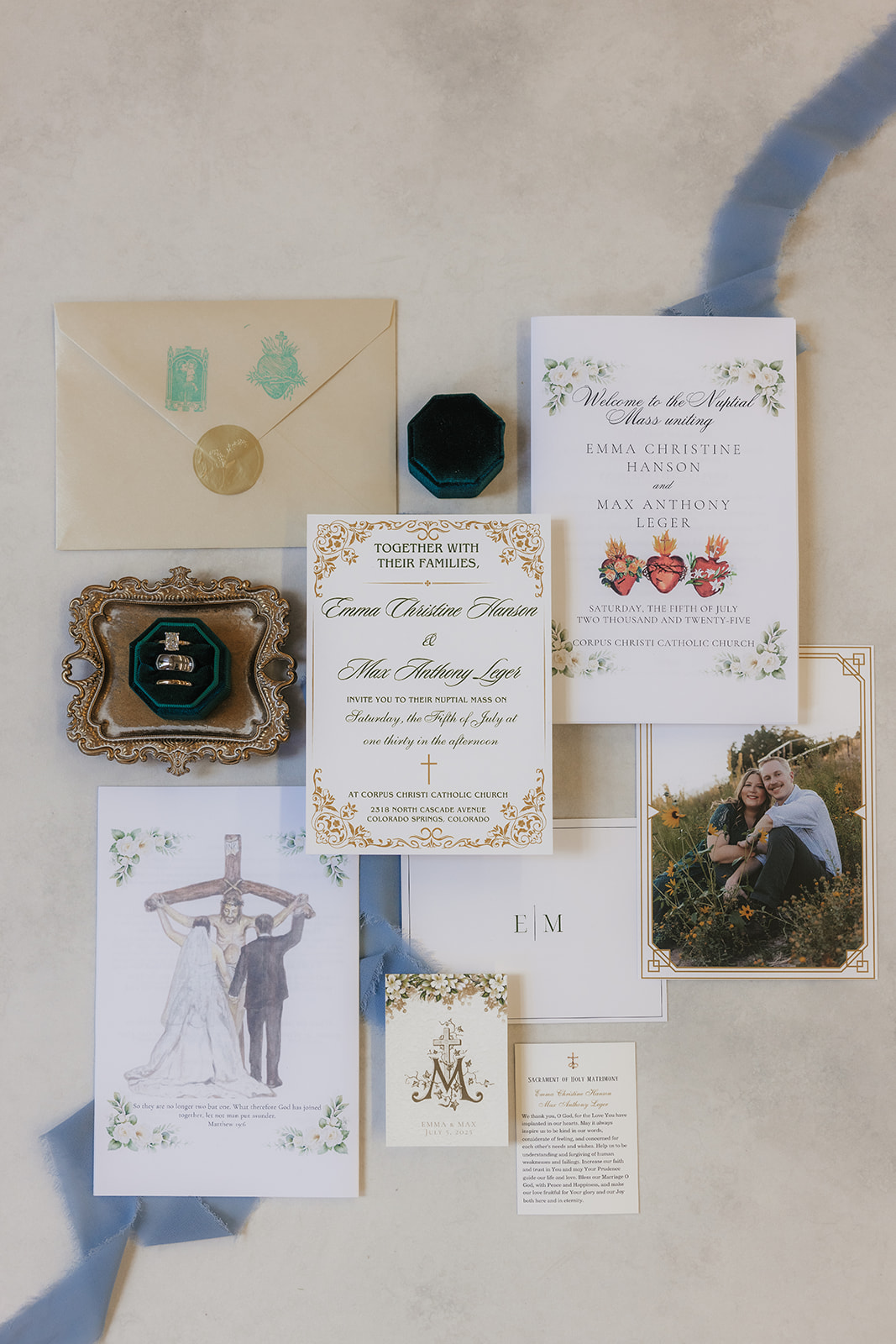 A flat lay of wedding invitations, envelopes, a photo of a couple, a small framed picture, a ring box, and printed wedding materials arranged on a light surface with a ribbon.