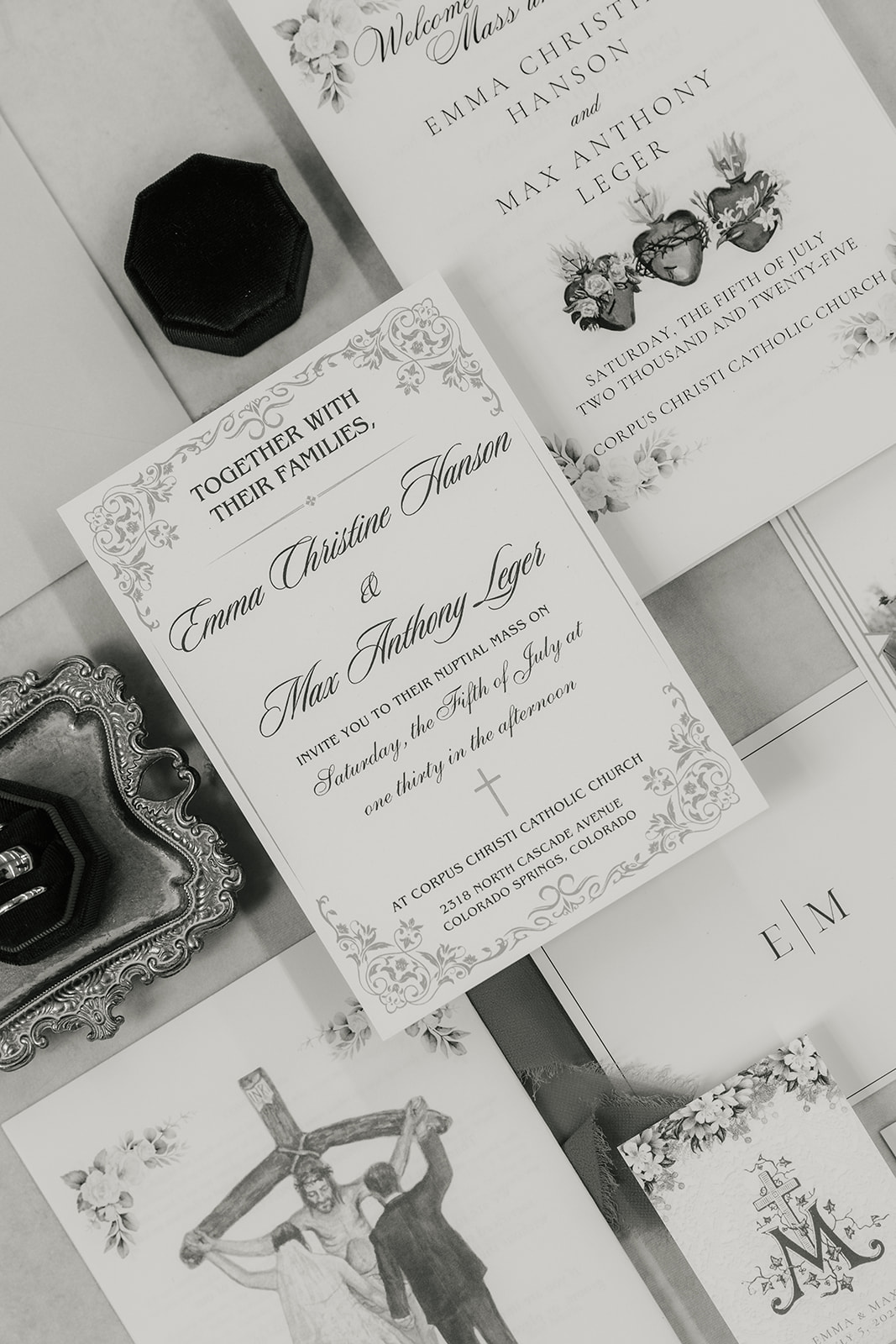 A flat lay of wedding invitations, envelopes, a photo of a couple, a small framed picture, a ring box, and printed wedding materials arranged on a light surface with a ribbon.