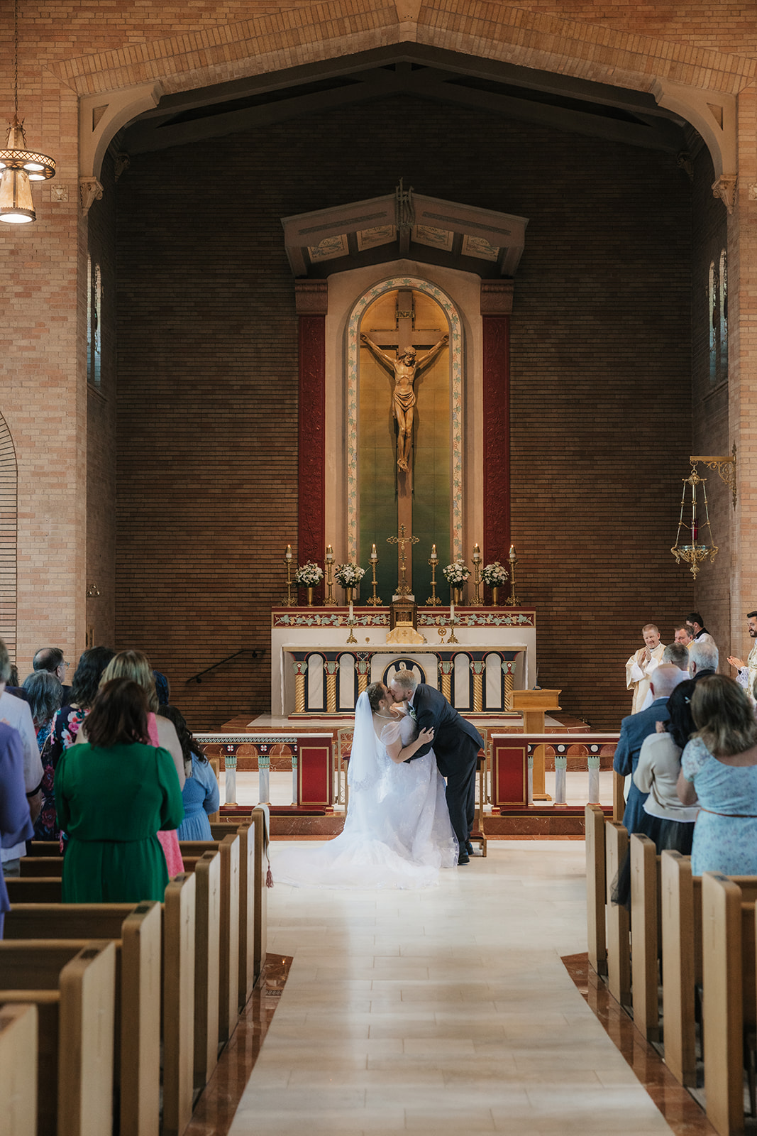 A wedding ceremony takes place in a church, with the bride and groom standing at the altar and guests seated in pews for catholic wedding photos