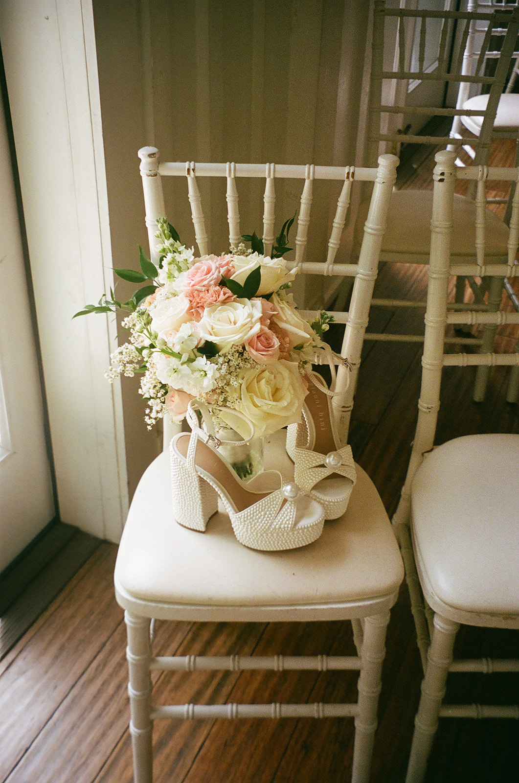 A pair of white high-heeled platform shoes with ankle straps hanging on a green leafy ivy backdrop.