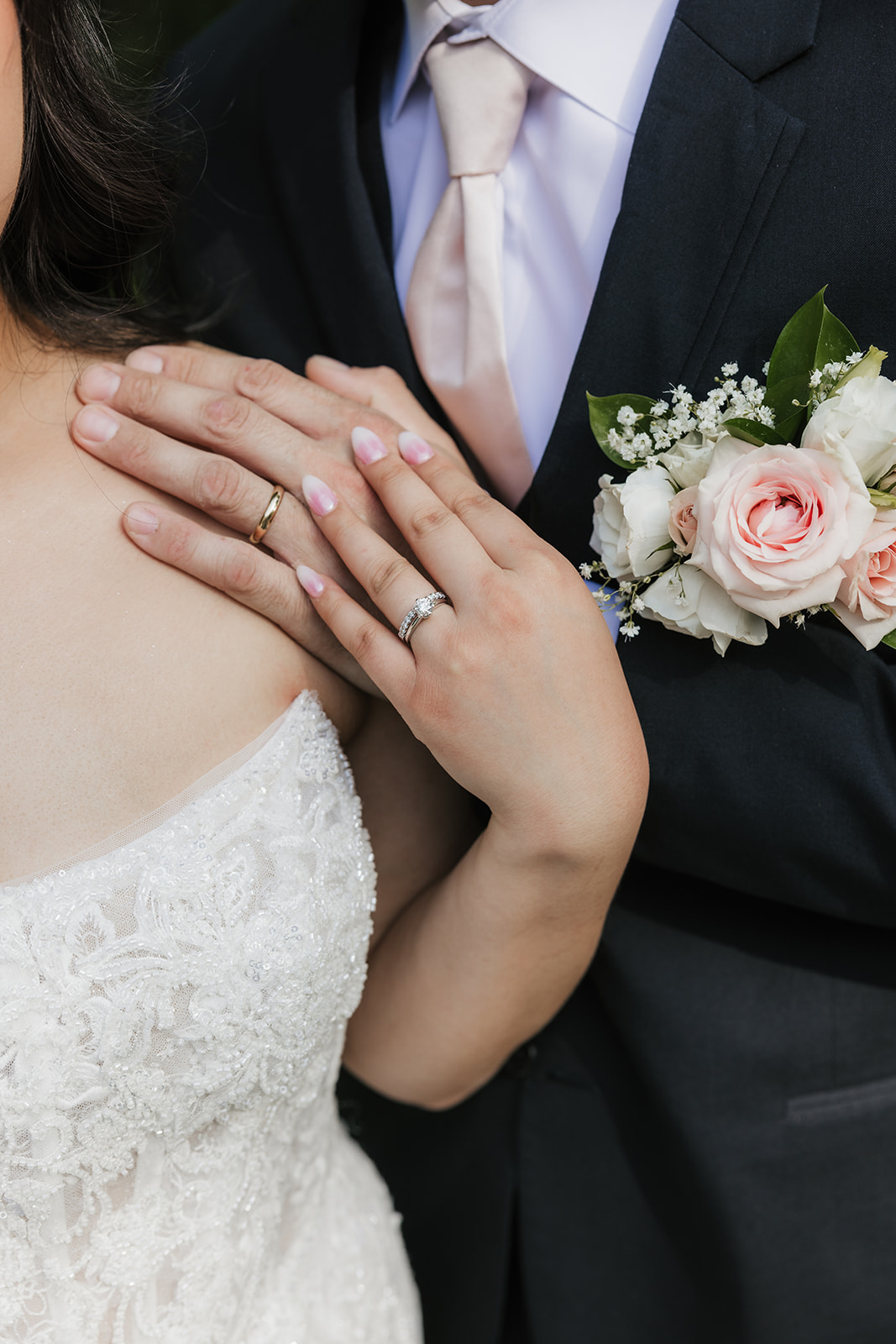 A bride and groom stand together outdoors on a stone path, surrounded by greenery. The bride holds a bouquet and wears a long white dress with a veil for a wedding at Spain Ranch