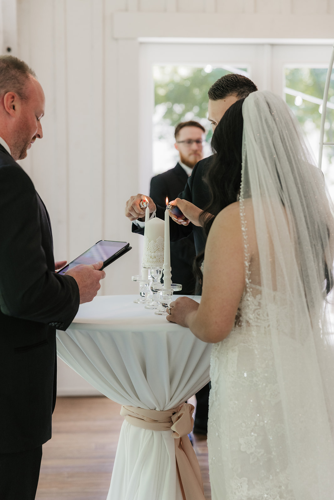 A bride and groom stand with an officiant under a floral arch indoors, exchanging vows during a wedding ceremony at spain ranch