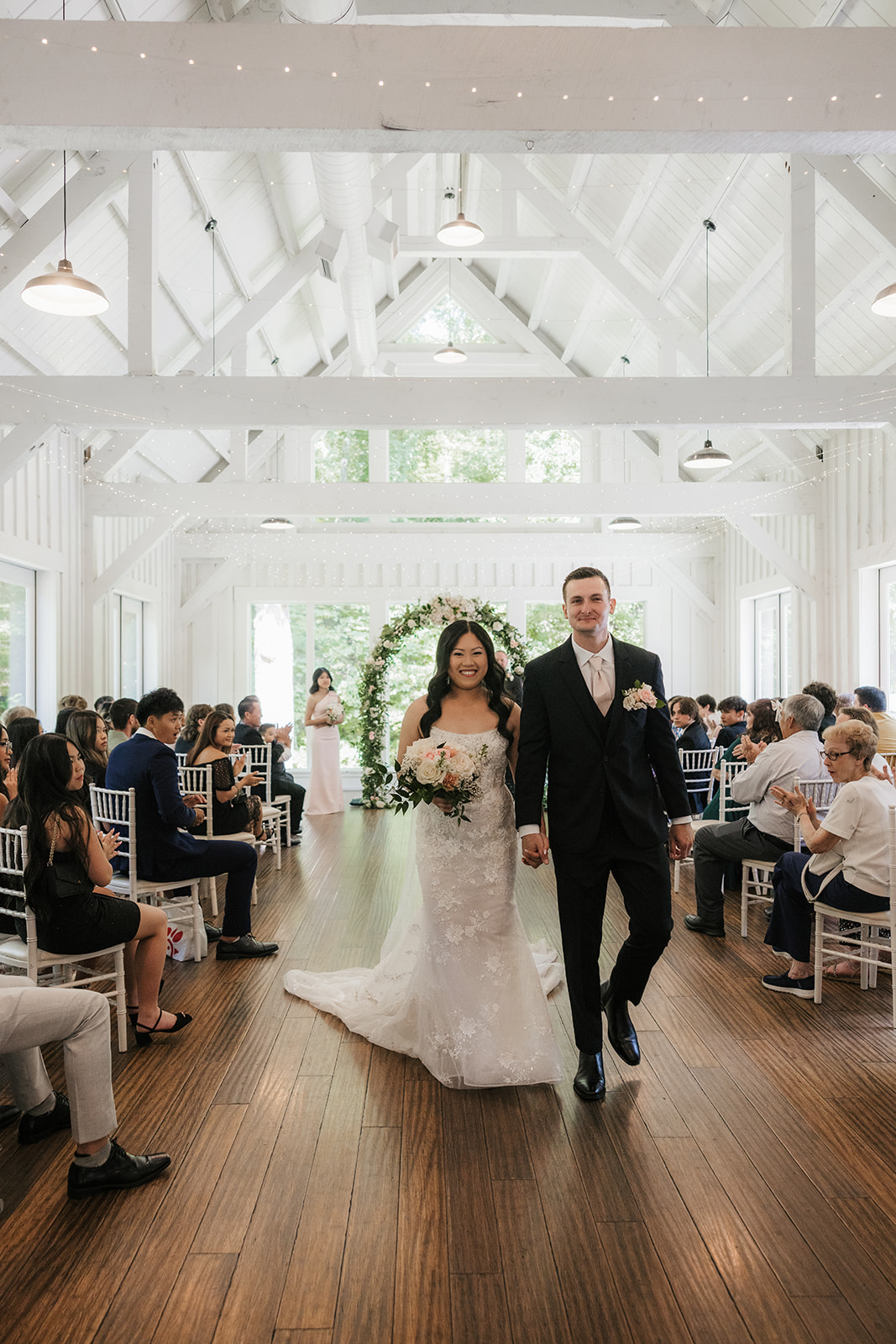 A bride and groom stand with an officiant under a floral arch indoors, exchanging vows during a wedding ceremony at spain ranch