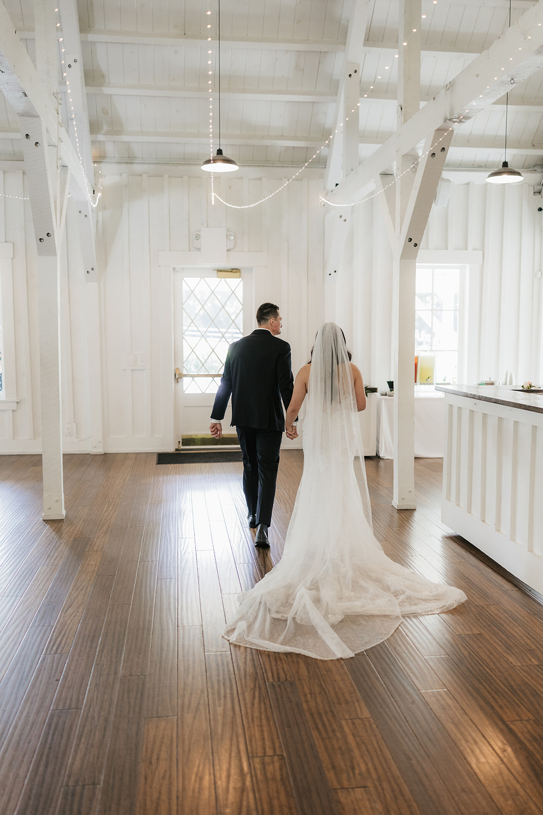 A bride and groom stand with an officiant under a floral arch indoors, exchanging vows during a wedding ceremony at spain ranch