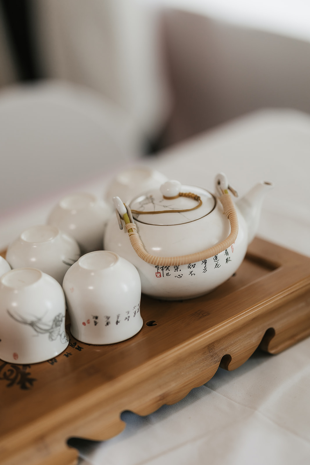 A white ceramic teapot with a bamboo handle and several matching cups are arranged on a wooden tray.