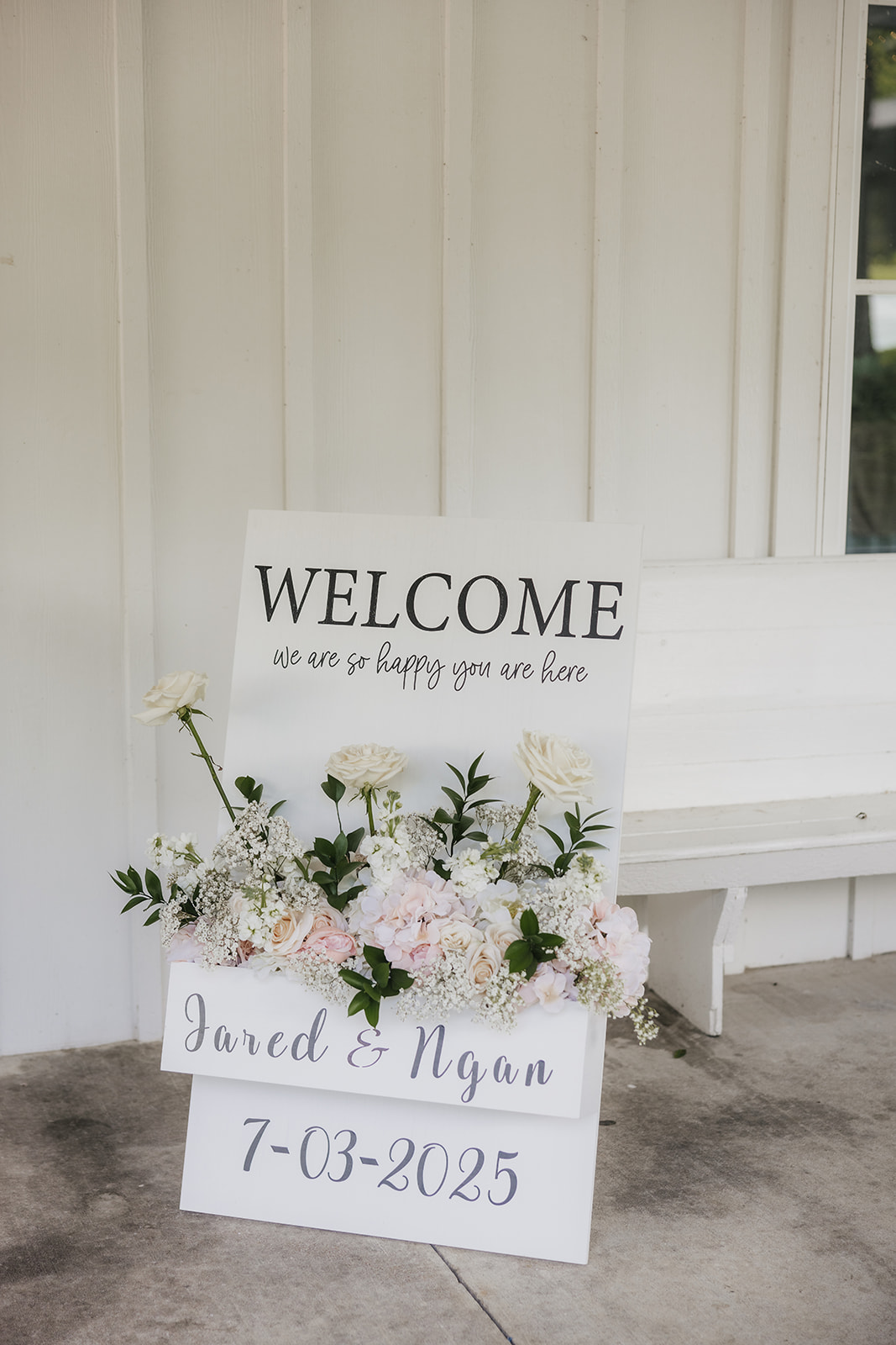 A bright, airy event space with white walls and wooden beams, featuring round tables set with white linens and floral centerpieces, arranged for a celebration for a wedding at spain ranch