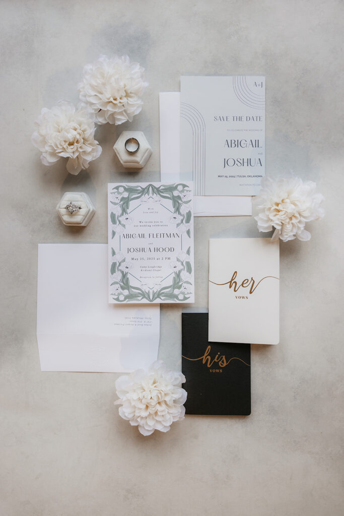 Flat lay of elegant wedding invitations, RSVP cards, envelopes, and white flowers arranged on a light surface.
