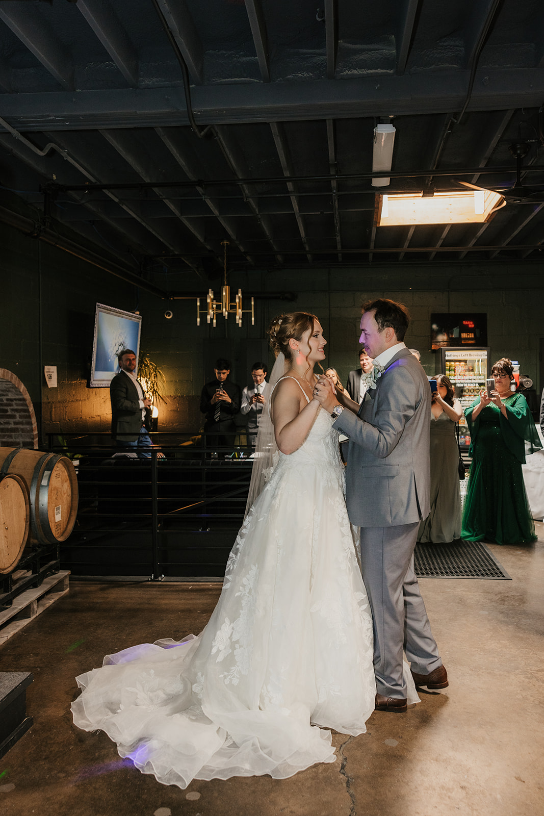 A bride and groom share a dance at their wedding reception indoors, with guests and decorations visible in the background at a Camp Loughridge Wedding