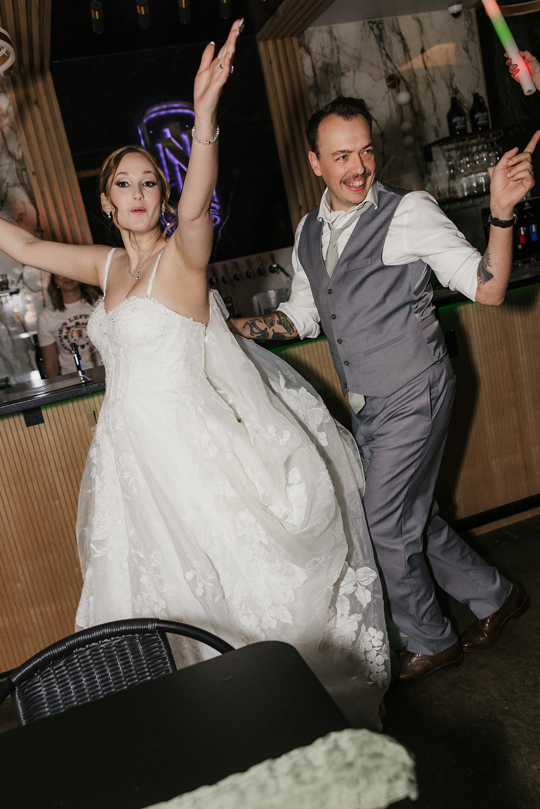 A bride and guests, holding light-up sticks, dance and celebrate together at an indoor wedding reception for a wedding at Camp Loughridge Wedding
