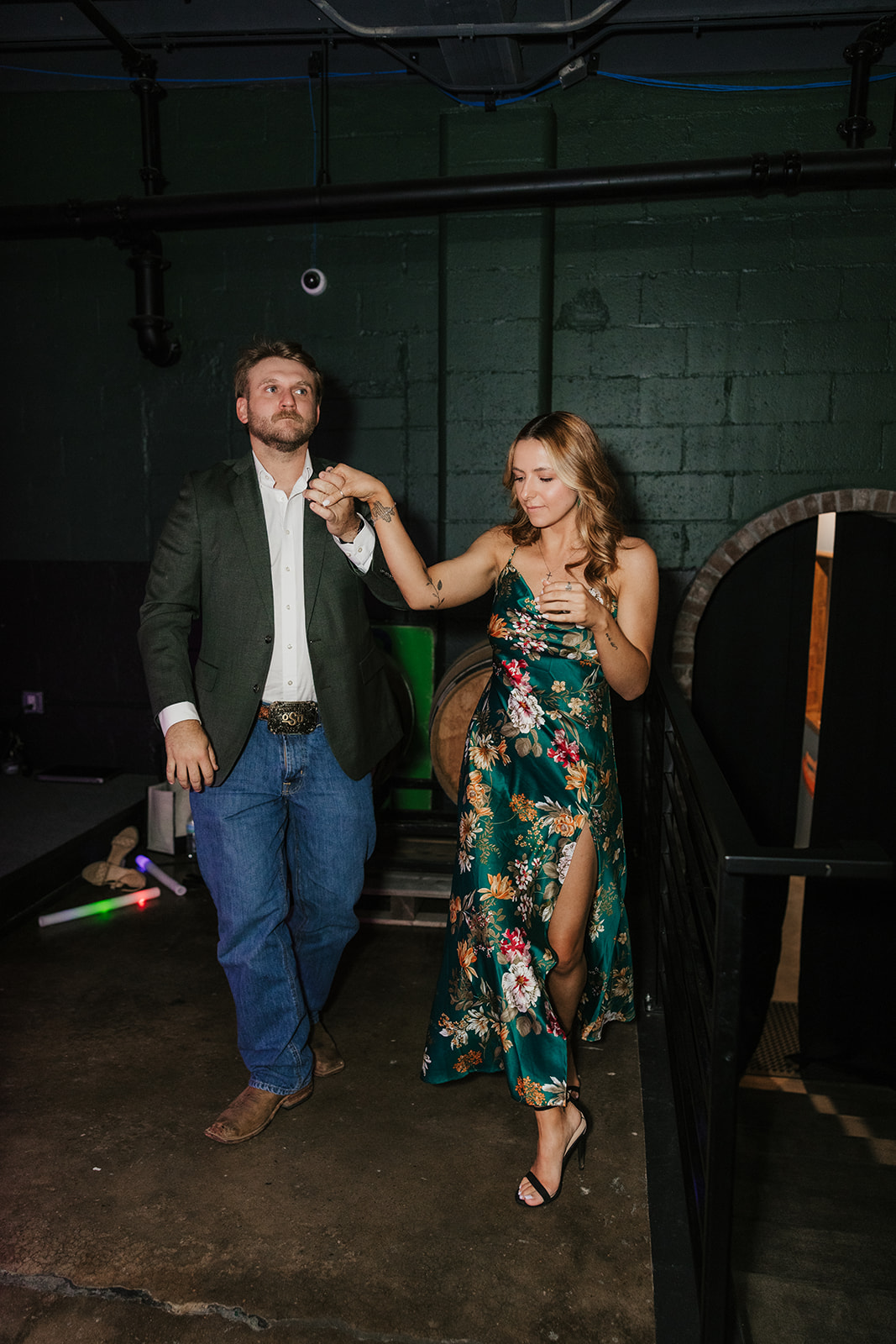 A bride and guests, holding light-up sticks, dance and celebrate together at an indoor wedding reception for a wedding at Camp Loughridge Wedding