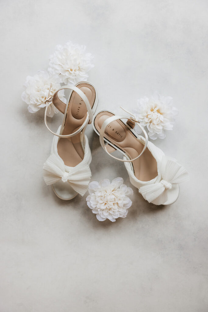 Flat lay of elegant wedding invitations, RSVP cards, envelopes, and white flowers arranged on a light surface.