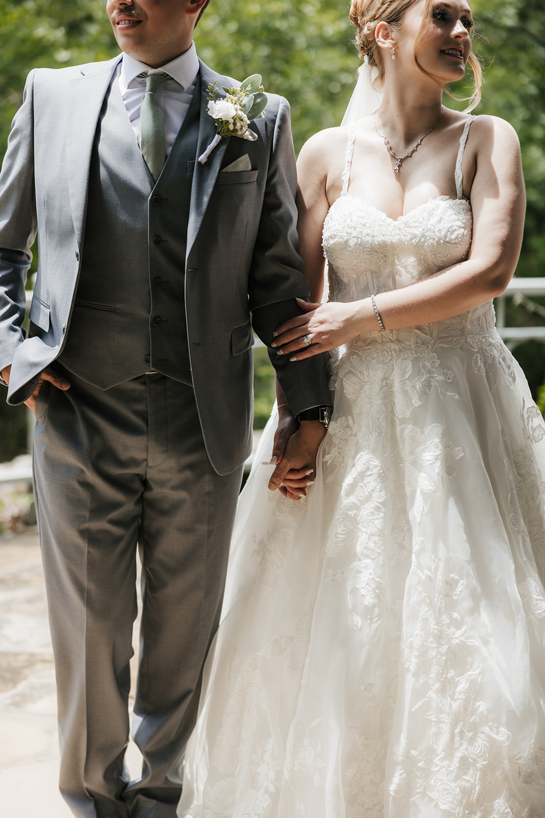 A bride and groom stand on a stone patio, sharing a kiss under the bride’s veil with trees and a metal railing in the background for a Camp Loughridge Wedding