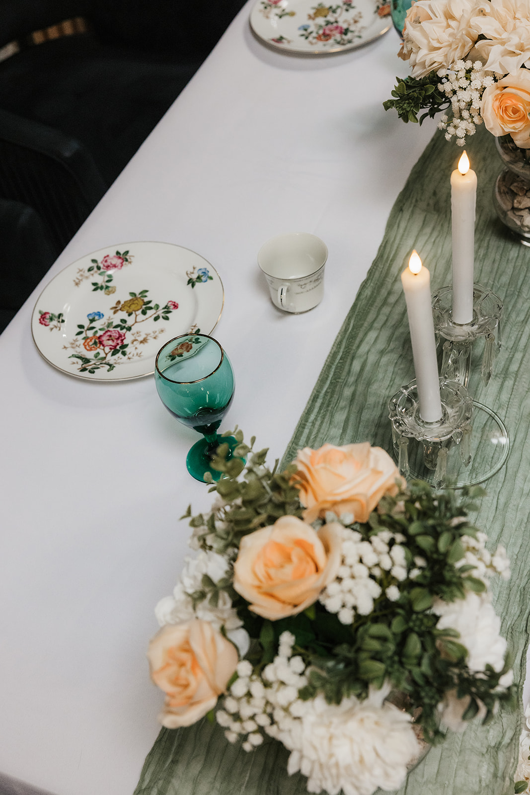 A decorated dining area with long wooden tables, floral centerpieces, green table runners, wall mirrors, and large flower artwork on the wall.
