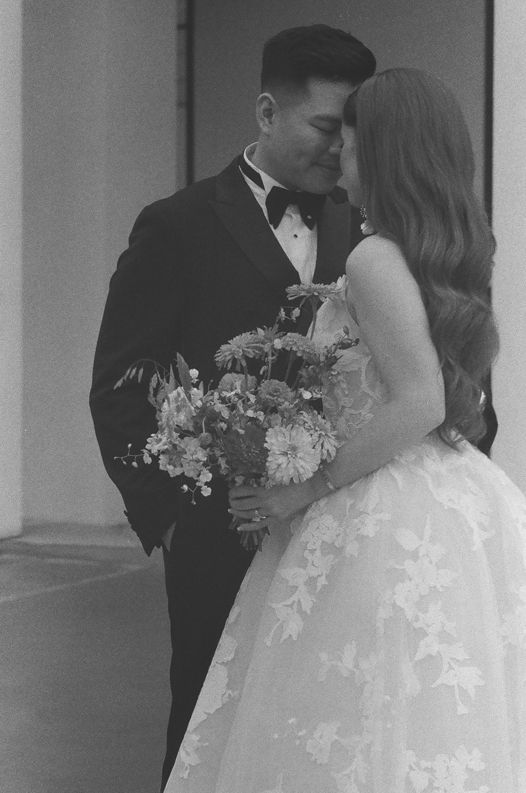 A couple dressed in formal attire, with the woman in a wedding gown, stands on a balcony looking outward in a black and white photo | unique wedding design