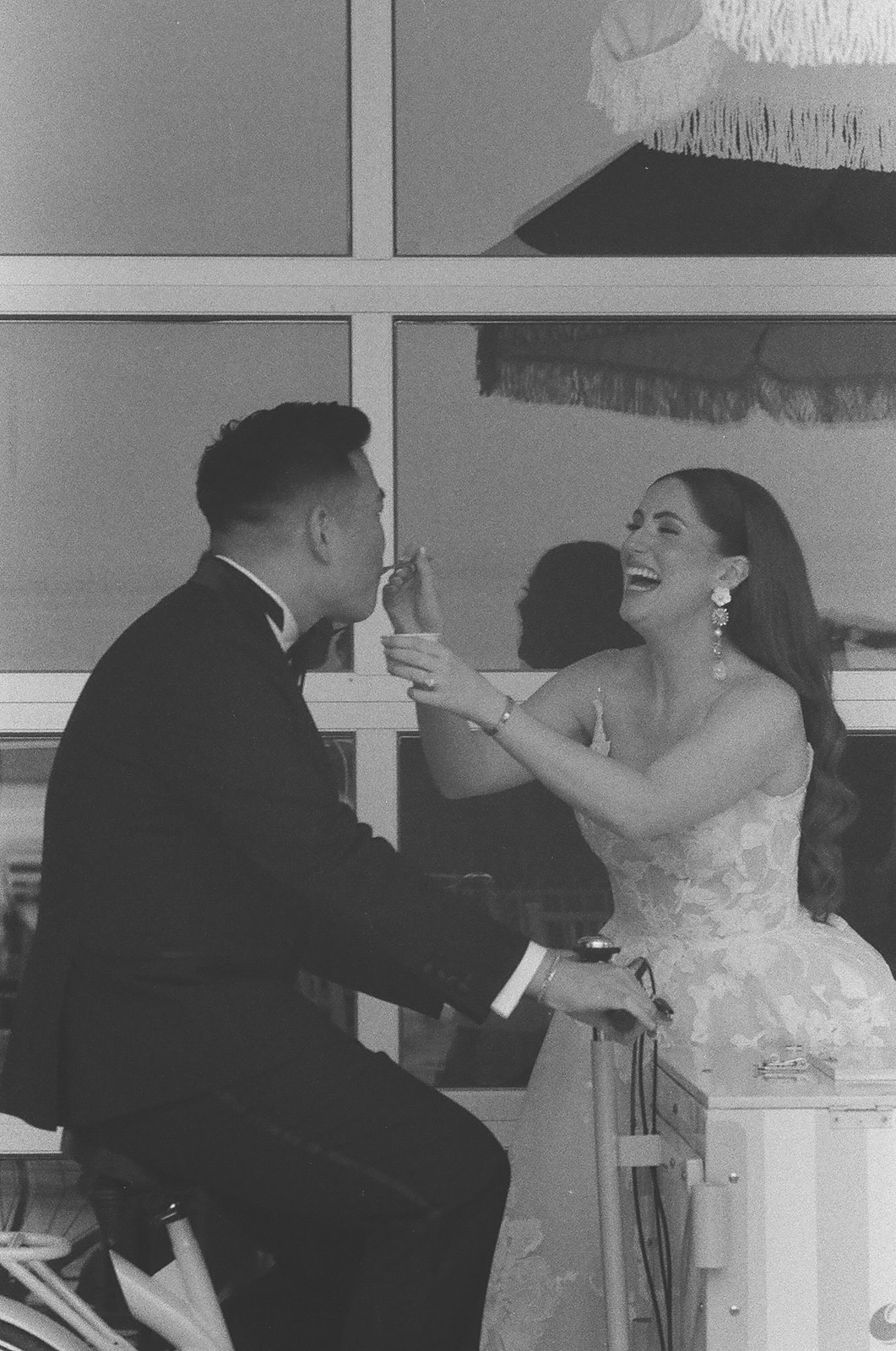 A couple dressed in formal attire, with the woman in a wedding gown, stands on a balcony looking outward in a black and white photo | unique wedding design