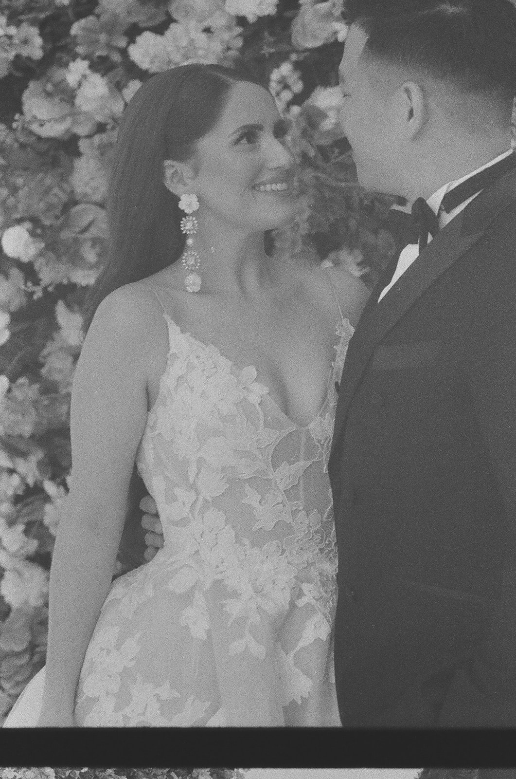 A couple dressed in formal attire, with the woman in a wedding gown, stands on a balcony looking outward in a black and white photo | unique wedding design