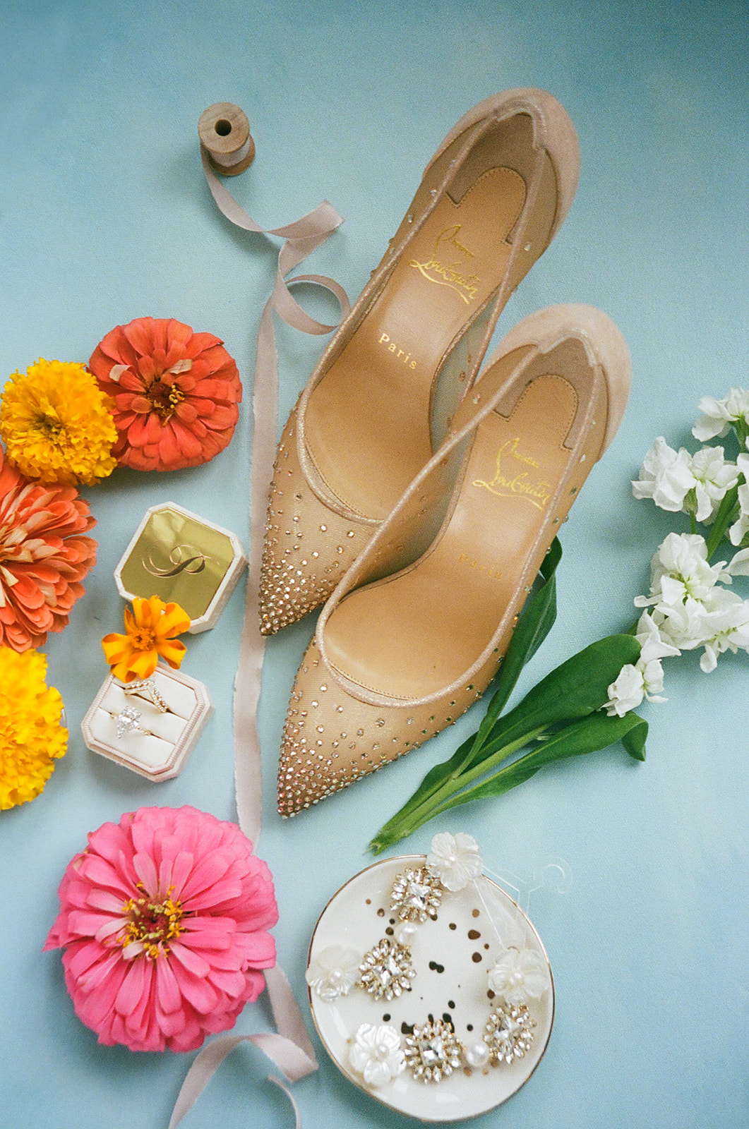 Flat lay of floral-themed stationery, place cards, a ribbon-tied invitation with a blue wax seal, yellow and orange flowers, and a green envelope on a floral fabric background. | unique wedding design