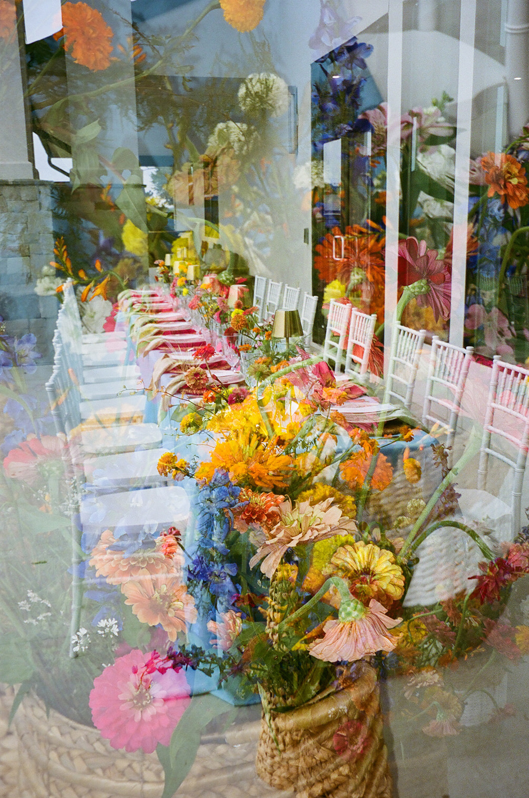 A long dining table with a light blue tablecloth, gold cups, glassware, and colorful flower arrangements is set outdoors beside a stone wall. | Unique wedding design