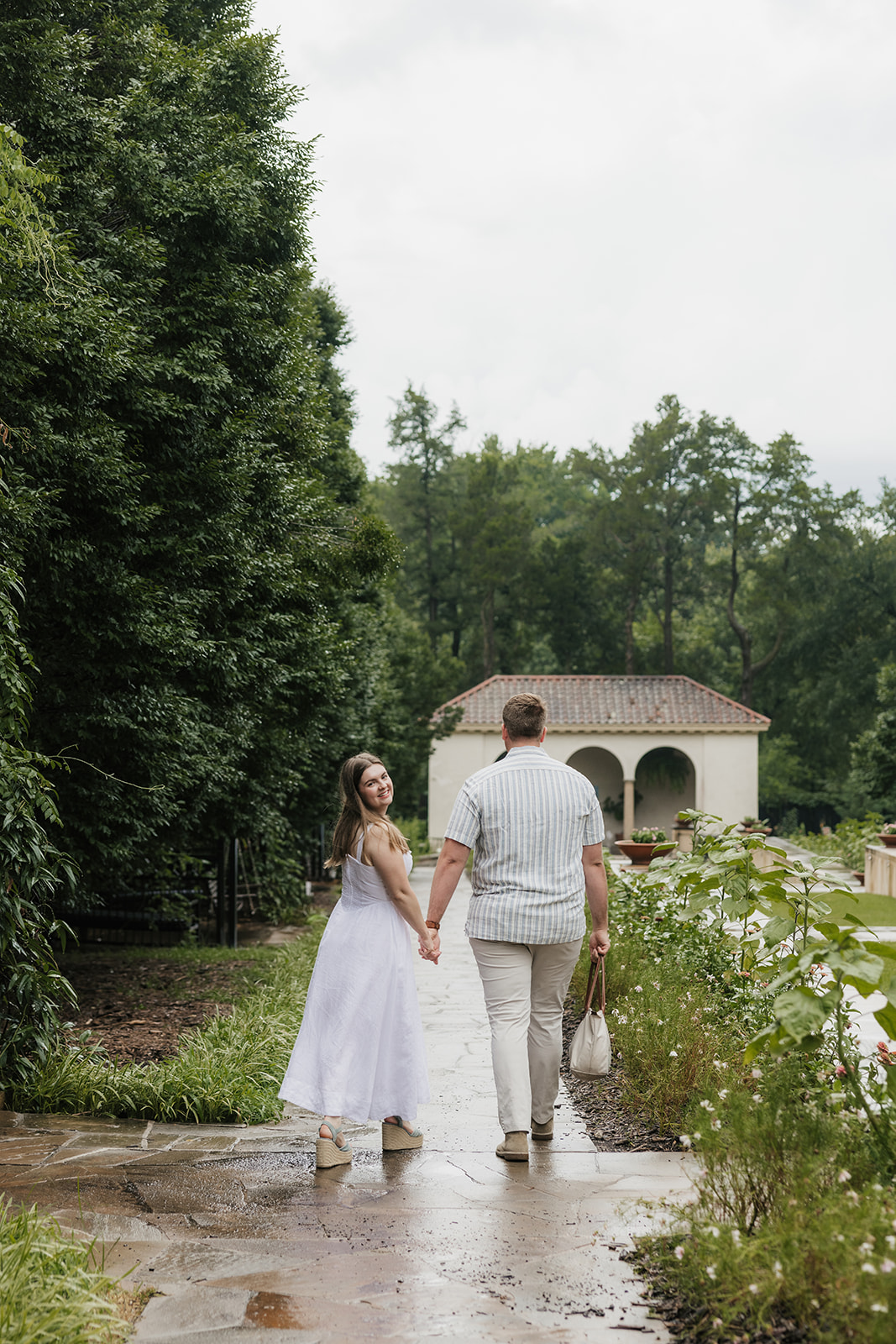 A bride and groom stand together on the steps of a large, elegant villa with tall windows and landscaped greenery at the Philbrook Museum in Tulsa Oklahoma