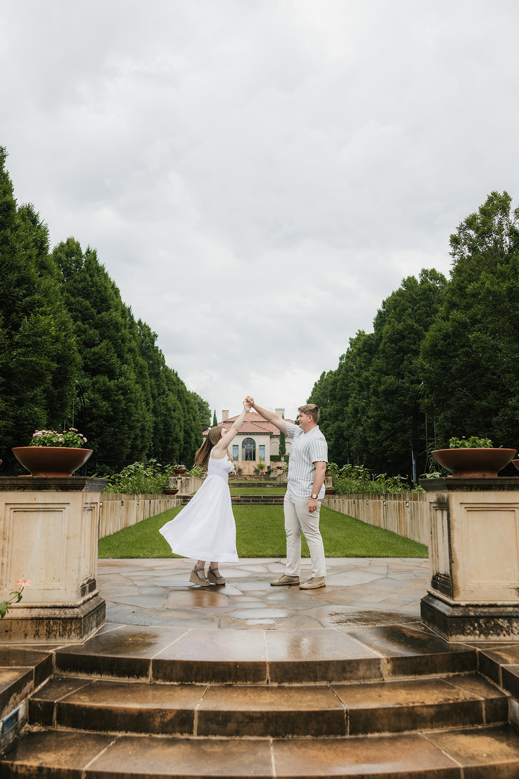 A bride and groom stand together on the steps of a large, elegant villa with tall windows and landscaped greenery at the Philbrook Museum in Tulsa Oklahoma