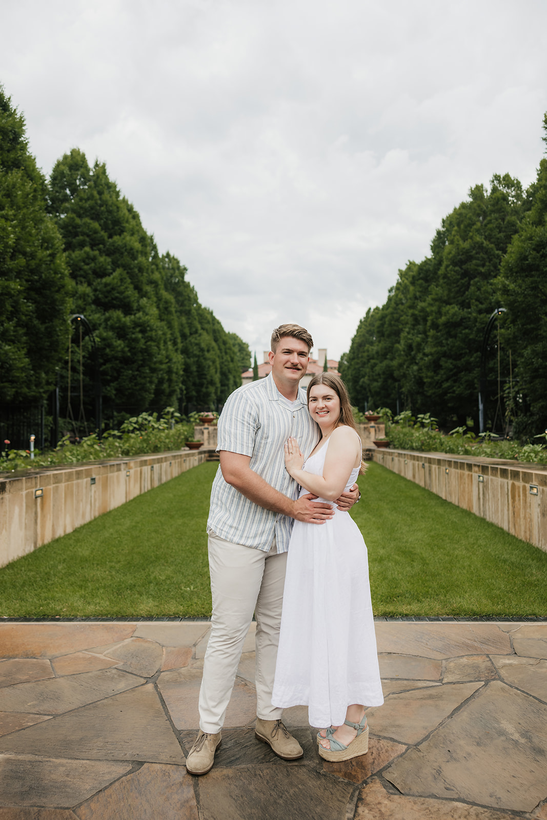 A bride and groom stand together on the steps of a large, elegant villa with tall windows and landscaped greenery at the Philbrook Museum in Tulsa Oklahoma