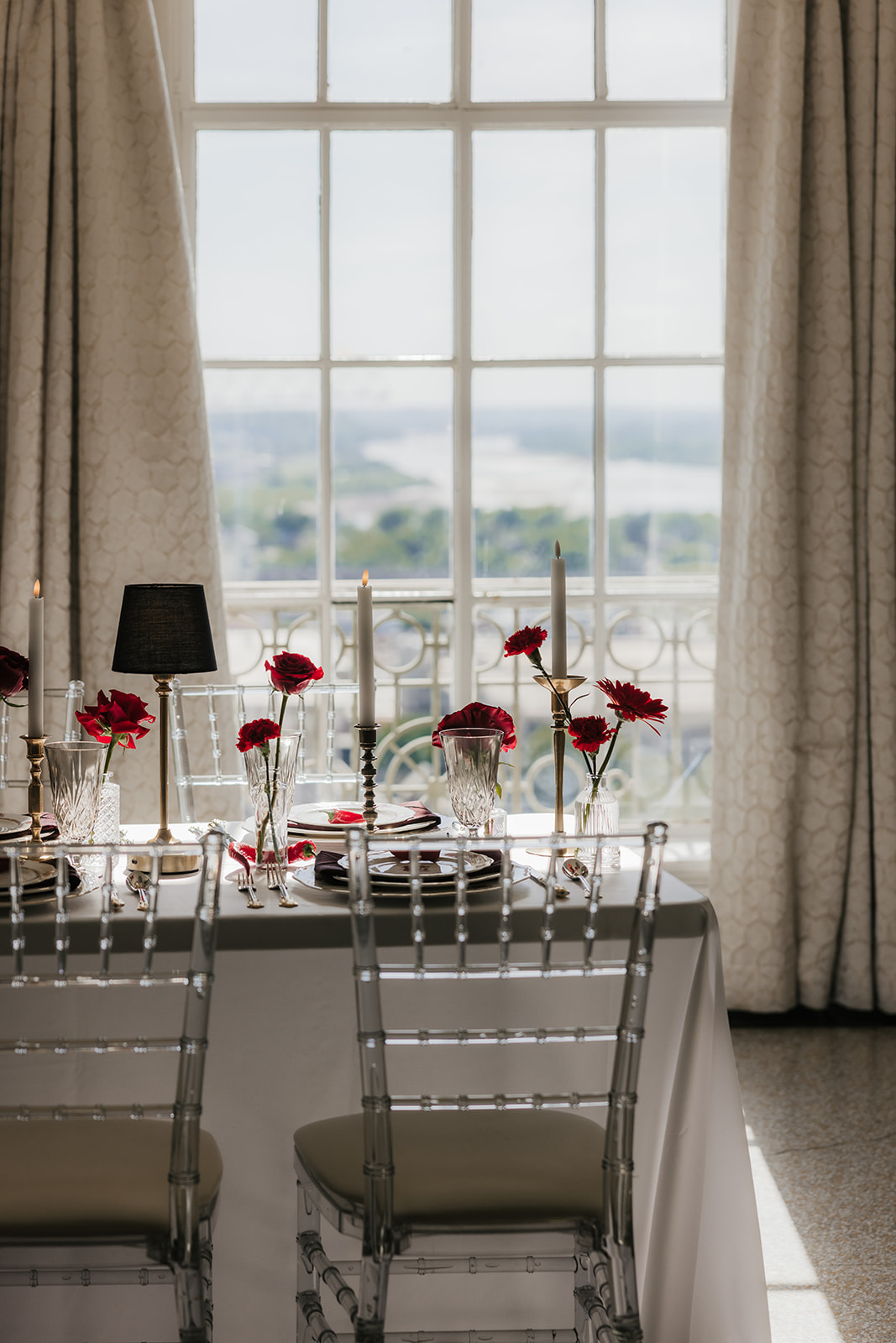 A formal table setting with stacked plates, crystal glassware, gold utensils, red napkin, a red chili pepper on the top plate, and red roses in vases on a white tablecloth for a Mayo Hotel wedding