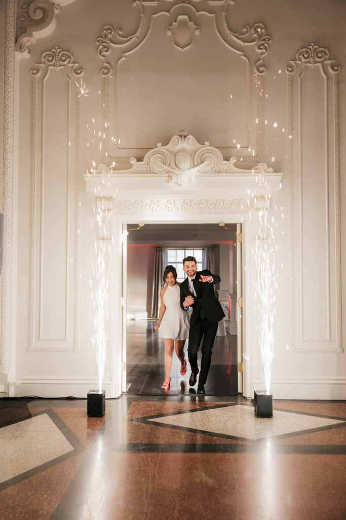 A couple dressed formally dances in a decorative room, with sparklers on each side of the doorway and natural light coming in from a window behind them for a mayo hotel wedding