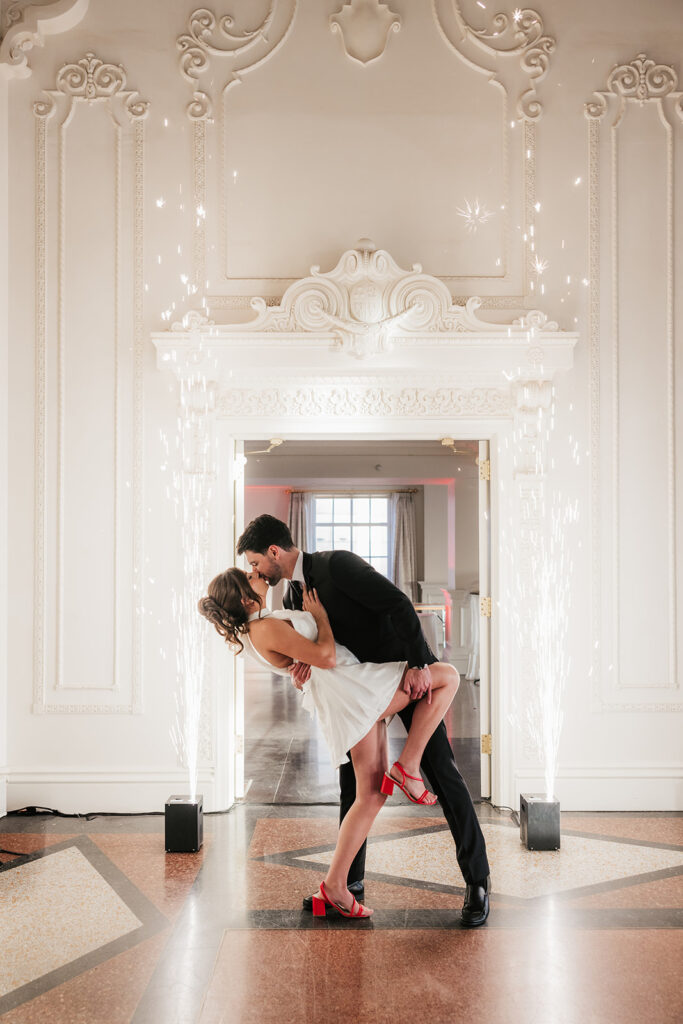 A couple dressed formally dances in a decorative room, with sparklers on each side of the doorway and natural light coming in from a window behind them for a mayo hotel wedding