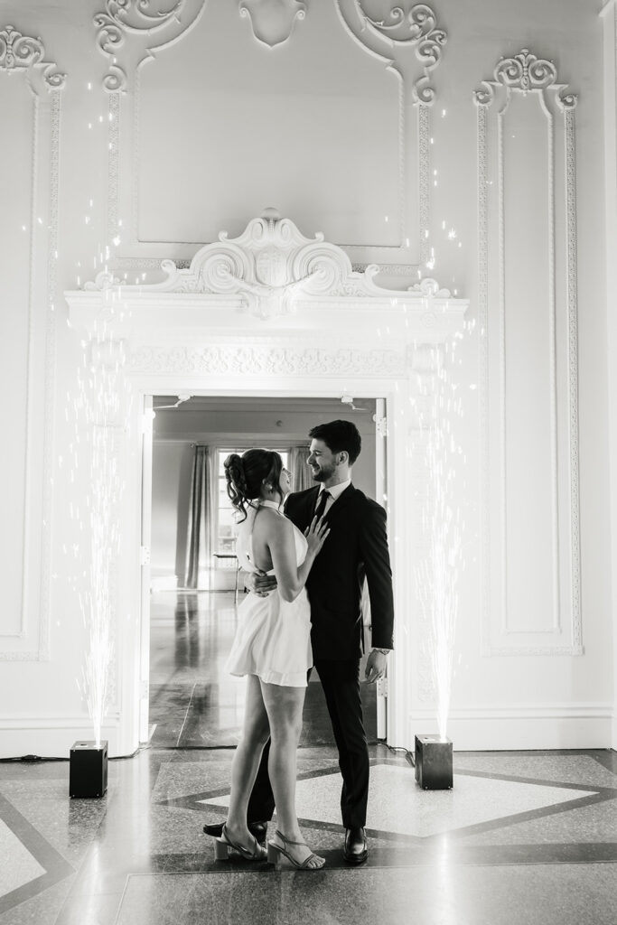 A couple dressed formally dances in a decorative room, with sparklers on each side of the doorway and natural light coming in from a window behind them for a mayo hotel wedding