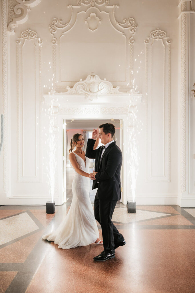 A couple dressed formally dances in a decorative room, with sparklers on each side of the doorway and natural light coming in from a window behind them for a mayo hotel wedding