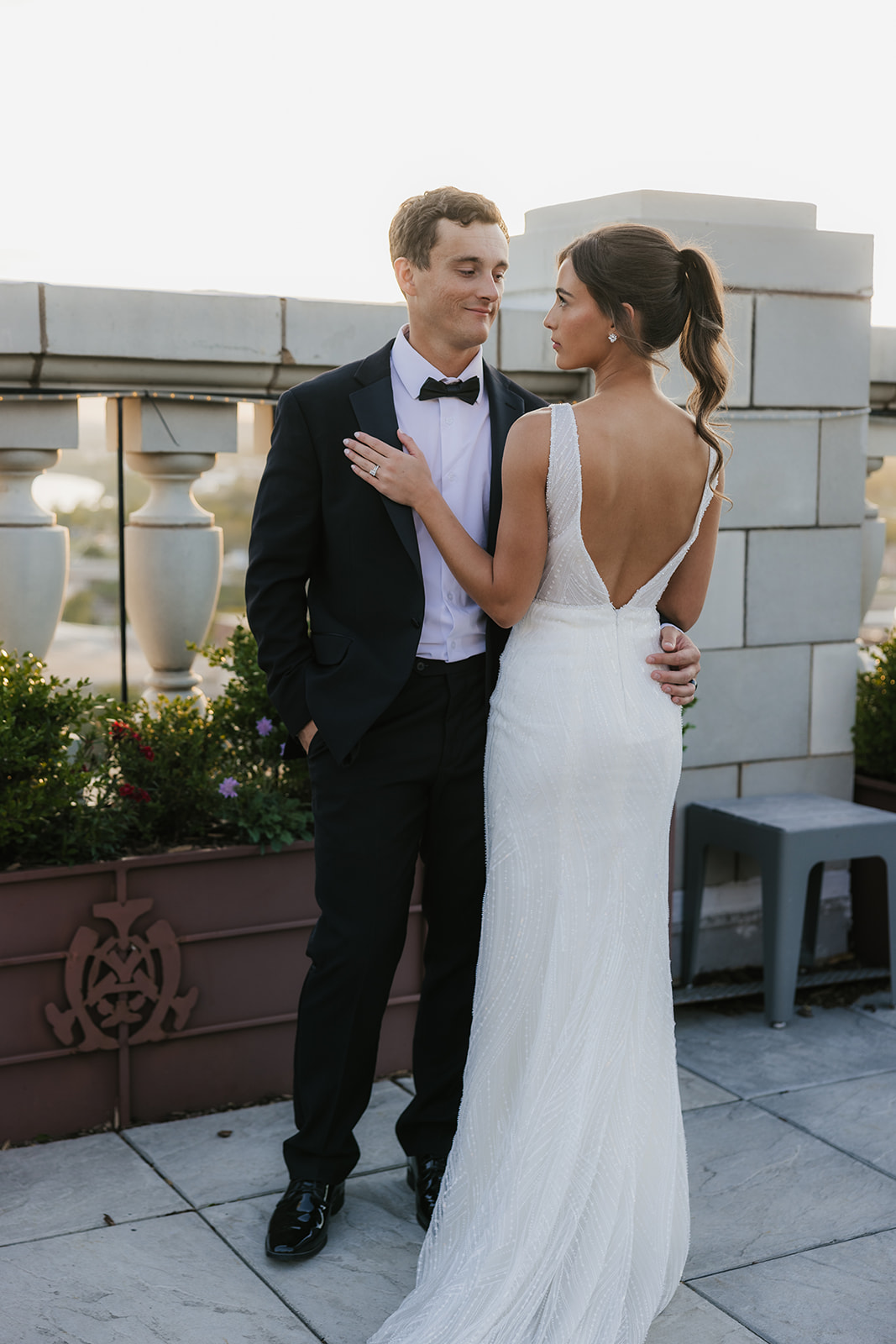 A bride in a white dress and a groom in a black suit stand close together on an outdoor terrace, looking at each other at the mayo hotel