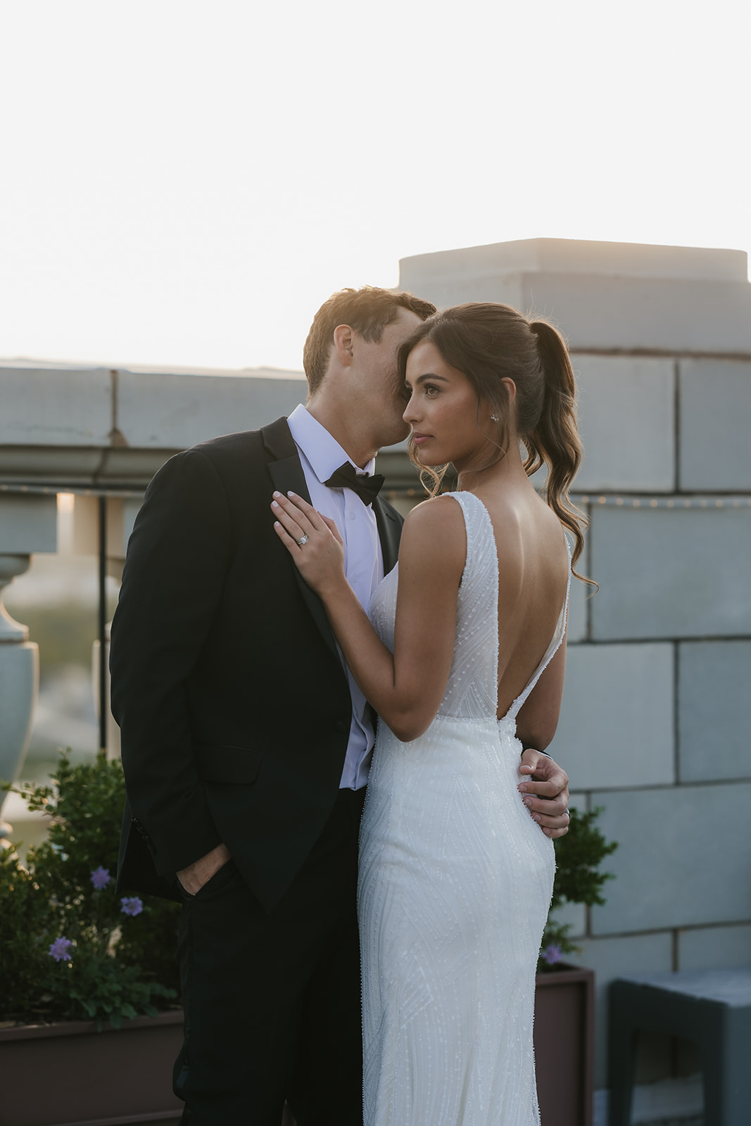A bride in a white dress and a groom in a black suit stand close together on an outdoor terrace, looking at each other at the mayo hotel