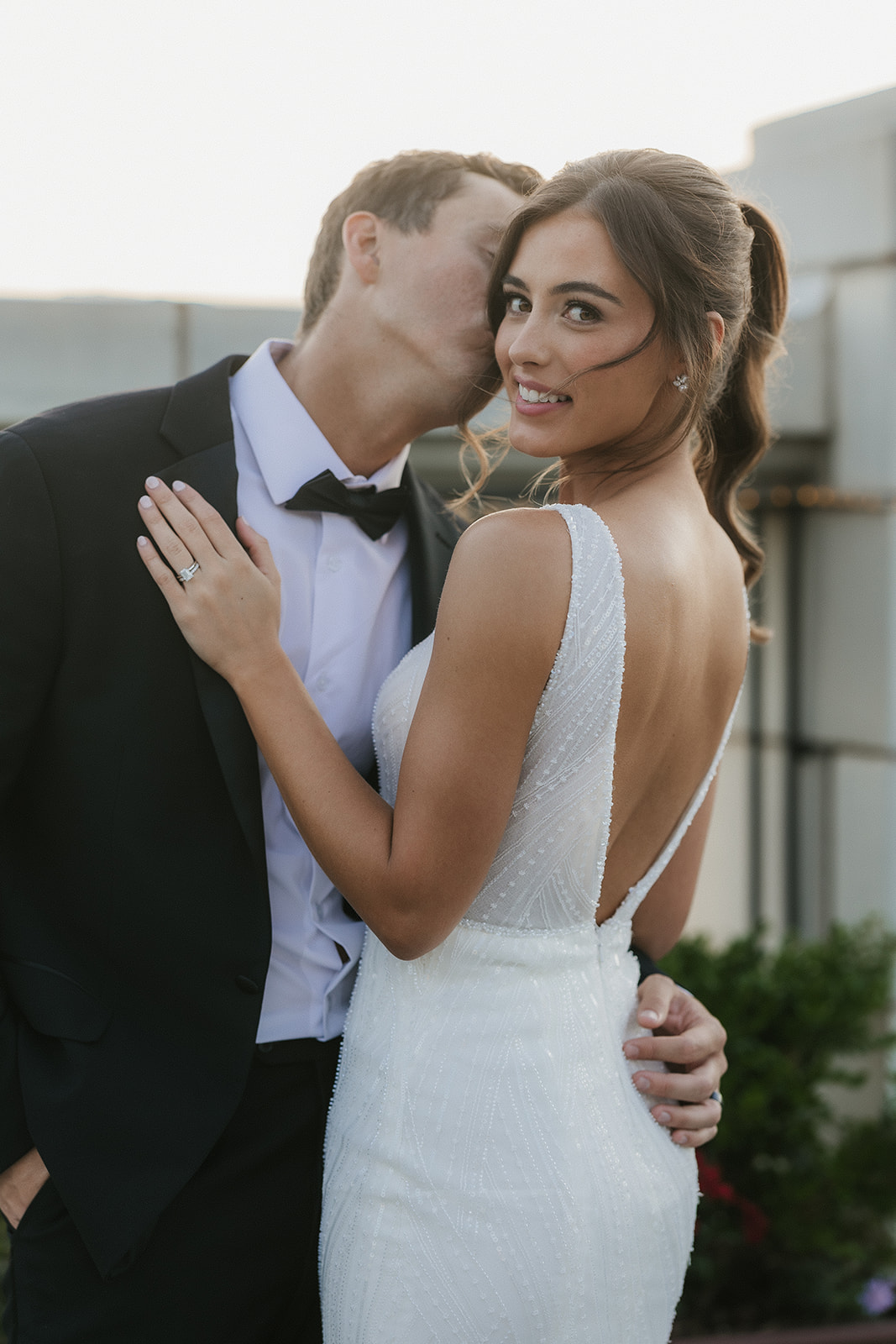 A bride in a white dress and a groom in a black suit stand close together on an outdoor terrace, looking at each other at the mayo hotel