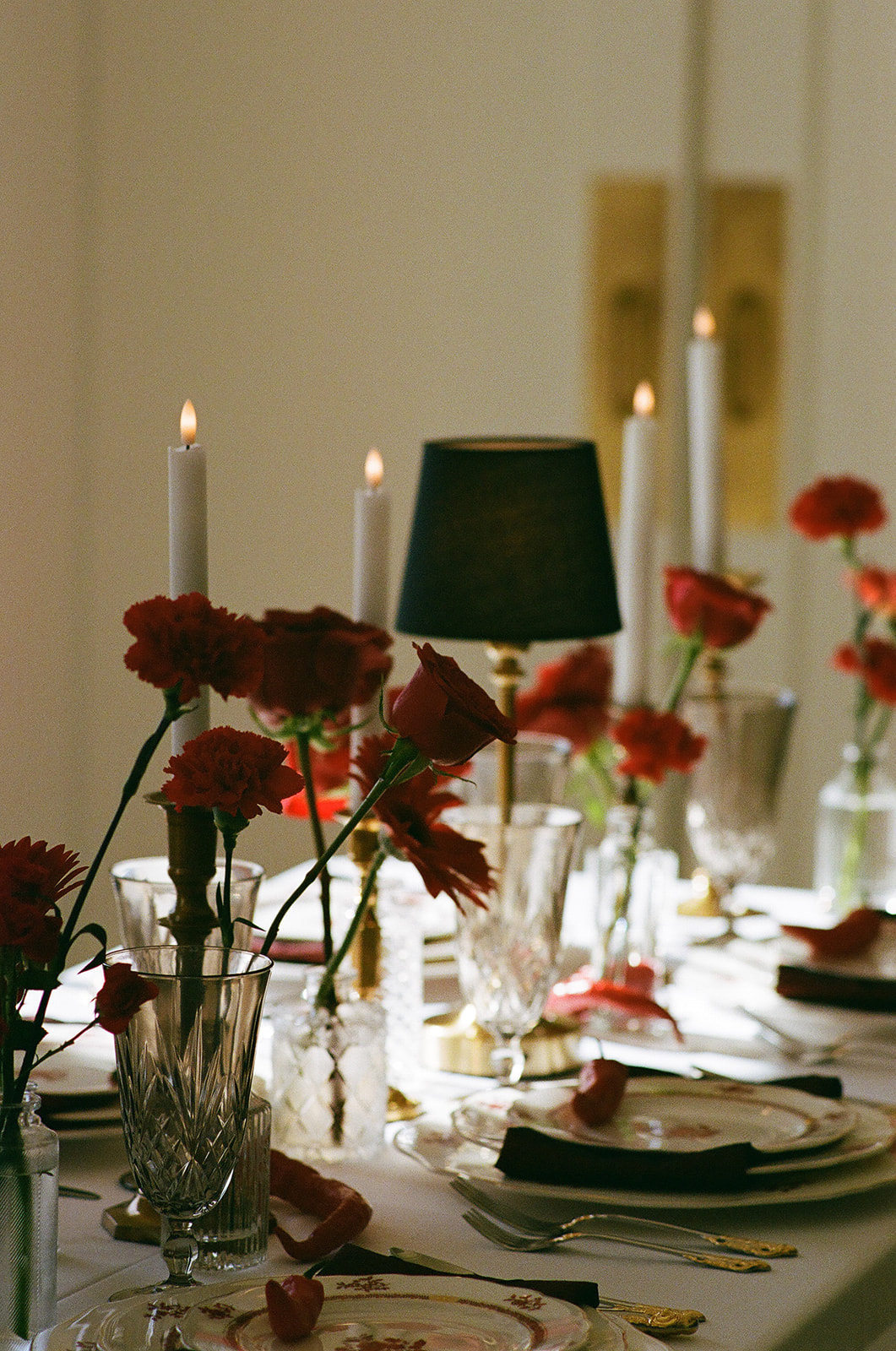 A formal table setting with stacked plates, crystal glassware, gold utensils, red napkin, a red chili pepper on the top plate, and red roses in vases on a white tablecloth for a Mayo Hotel wedding