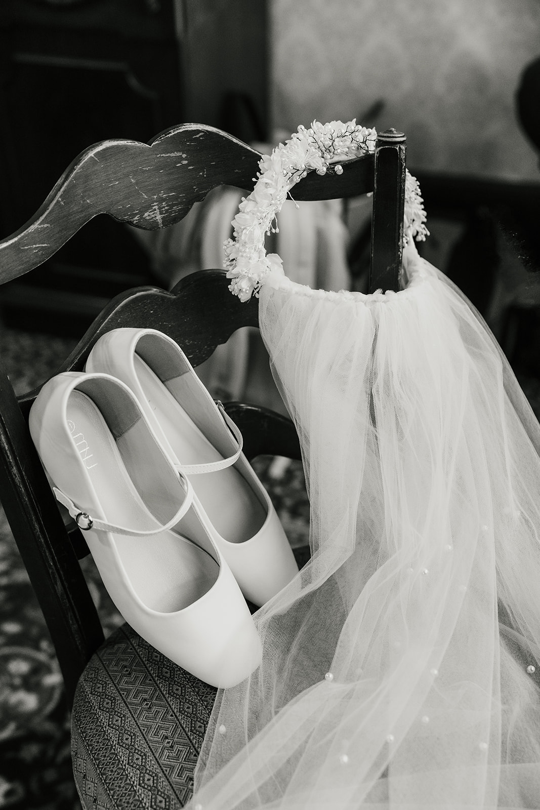 White shoes, a pearl necklace, a rosary, a ring in a blue box, a small perfume bottle, and a pin arranged on an upholstered chair.