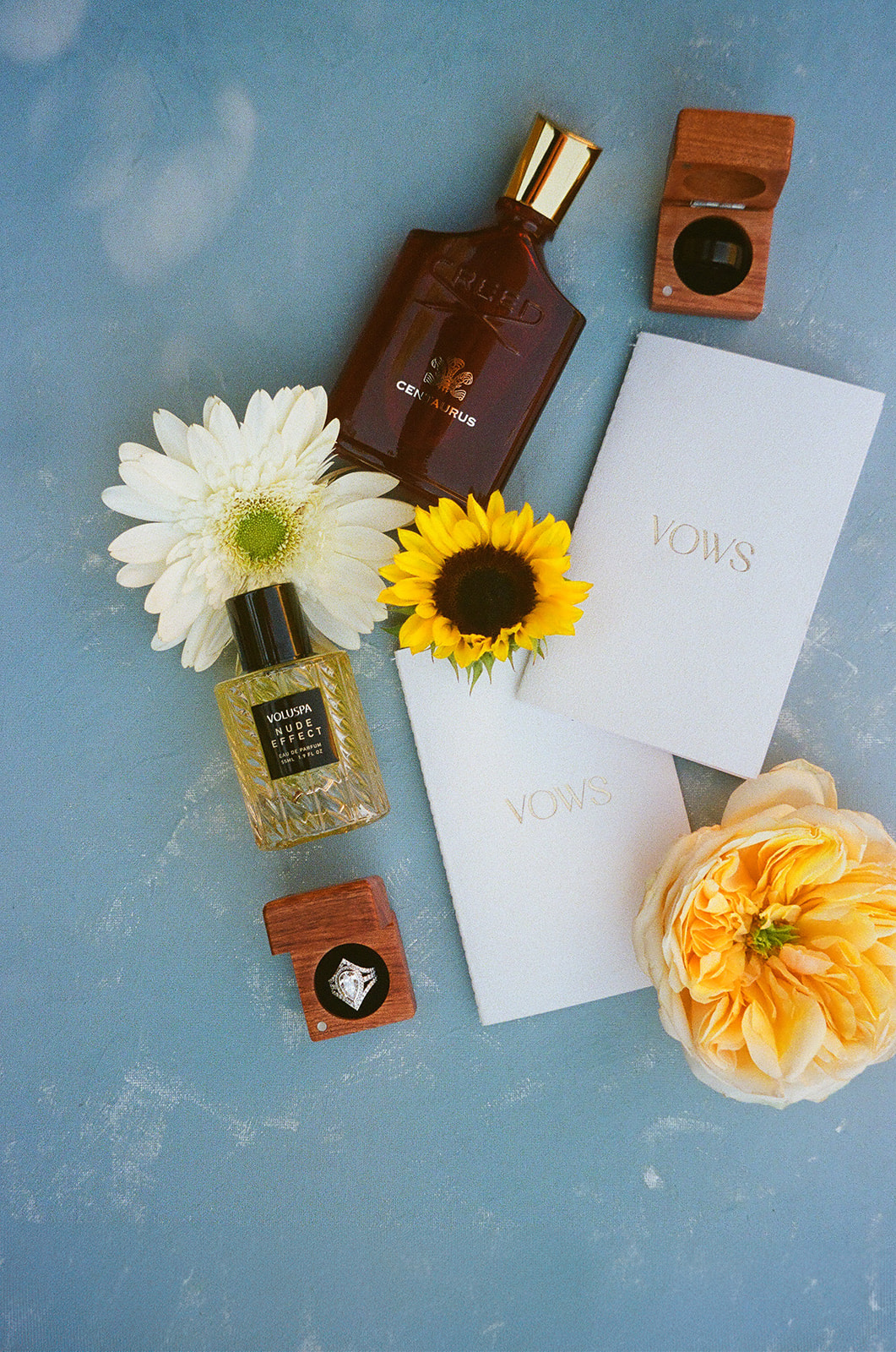 A wedding invitation with a photo of a couple is surrounded by flowers and two white booklets labeled “Vows” in gold lettering for a wedding at The Silo Event Center in Tulsa