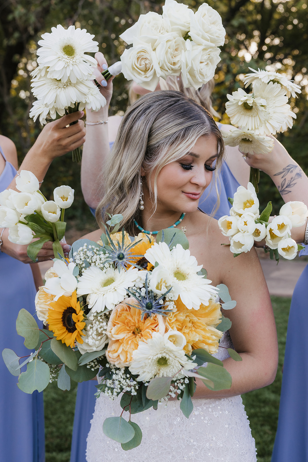 A bride in a white gown stands outdoors with four bridesmaids in matching light blue dresses, all holding bouquets and smiling at the Silo Event Center in Tulsa