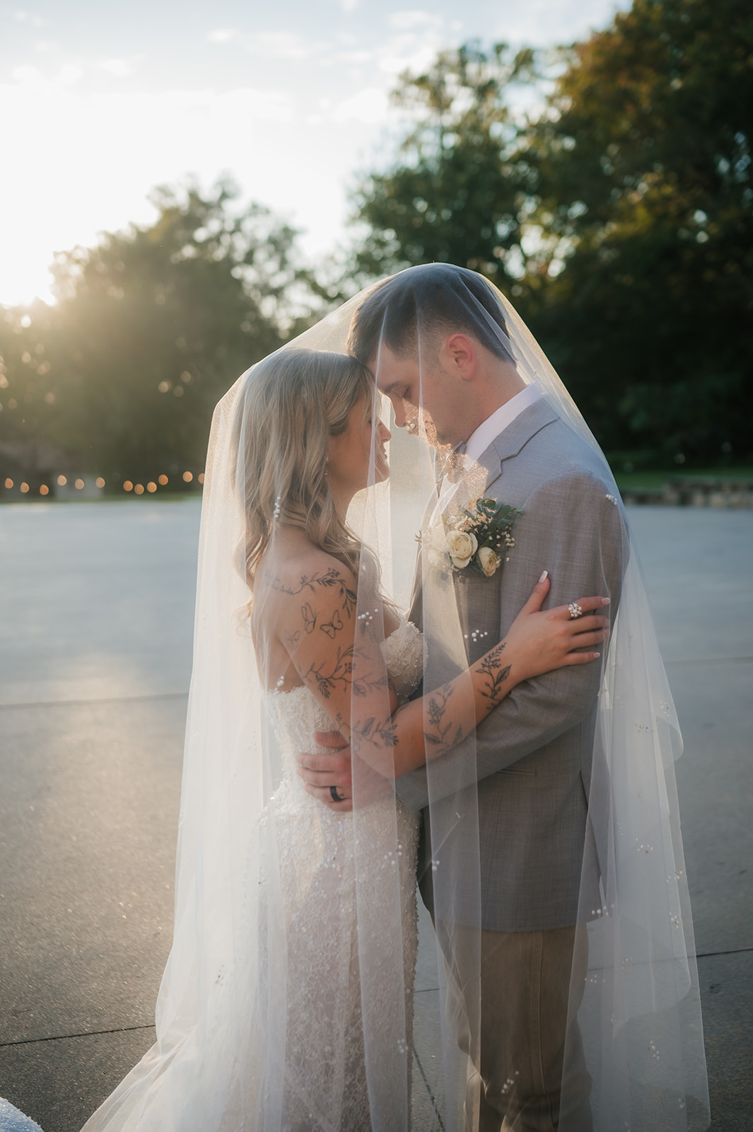 A bride and groom kiss under a white wooden pergola with a chandelier, surrounded by greenery on a circular platform at The Silo Event Center in Tulsa