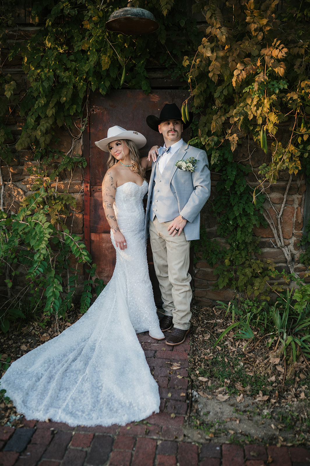 A bride and groom kiss under a white wooden pergola with a chandelier, surrounded by greenery on a circular platform at The Silo Event Center in Tulsa