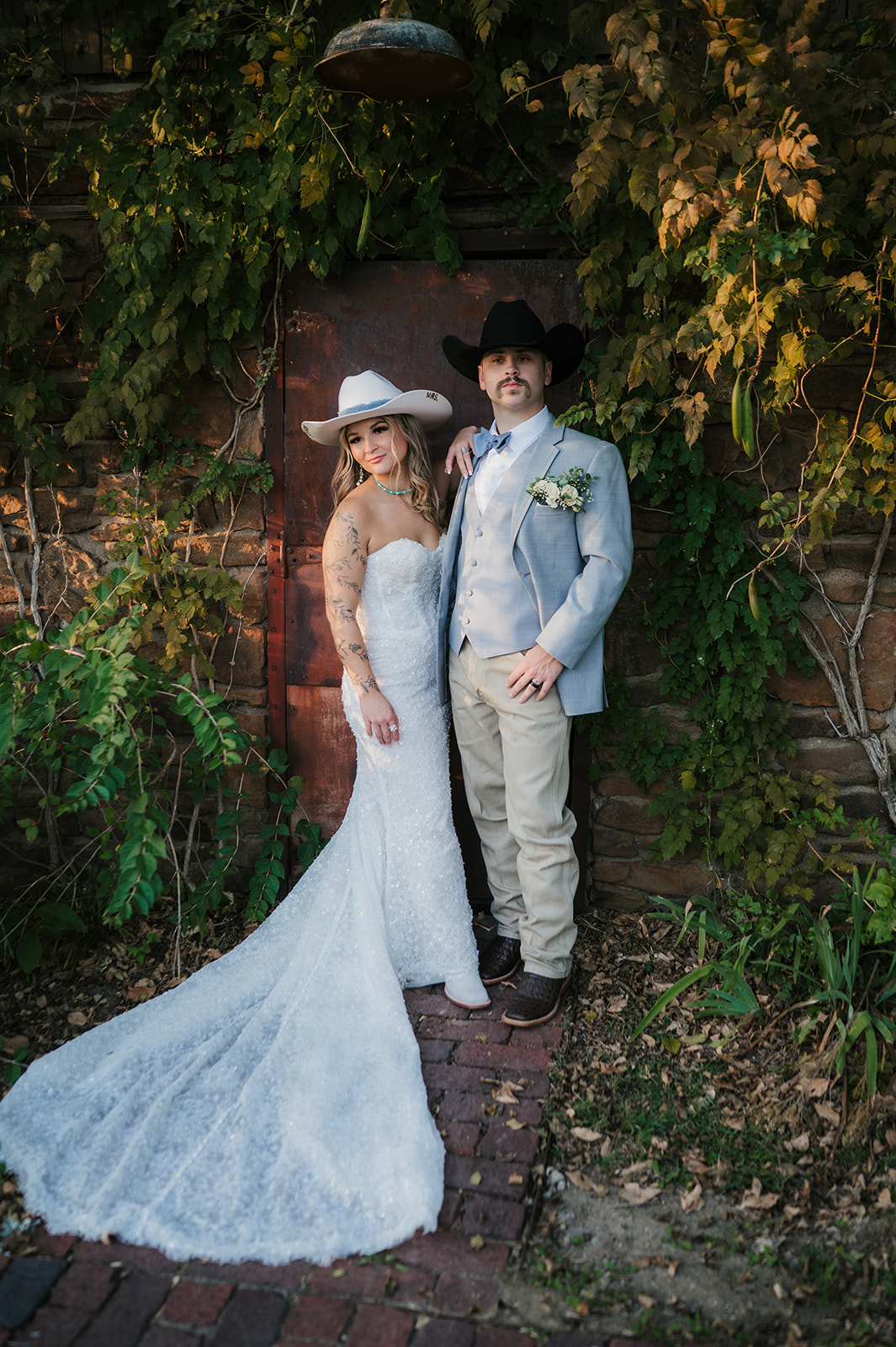 A bride and groom stand close together under a flowing veil outdoors; the bride wears a white dress and the groom a light gray suit with a floral boutonniere at aWedding at The Silo Event Center in Tulsa