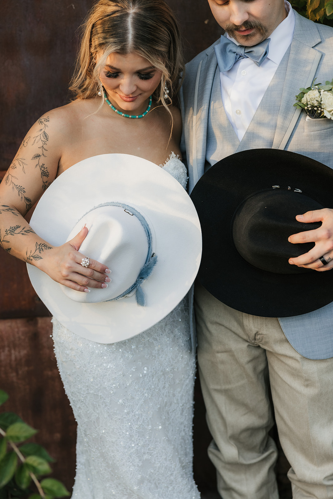 A bride and groom kiss under a white wooden pergola with a chandelier, surrounded by greenery on a circular platform at The Silo Event Center in Tulsa