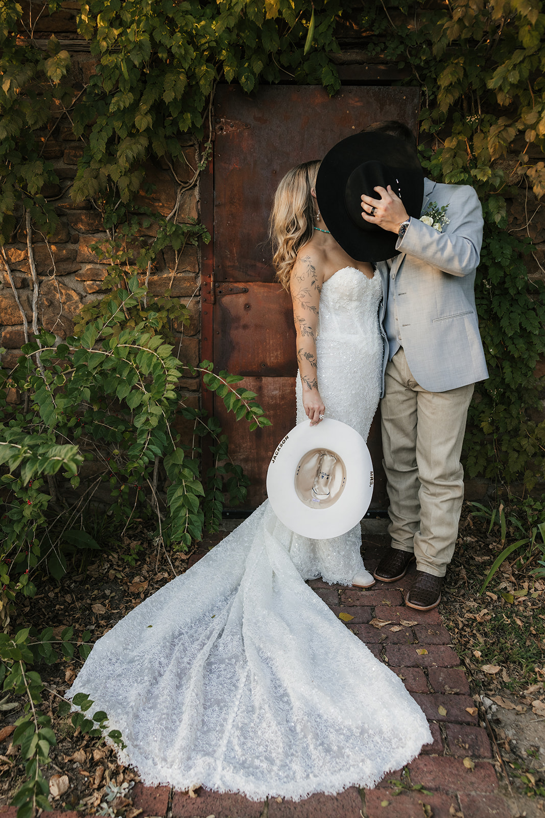A bride and groom stand close together under a flowing veil outdoors; the bride wears a white dress and the groom a light gray suit with a floral boutonniere at aWedding at The Silo Event Center in Tulsa