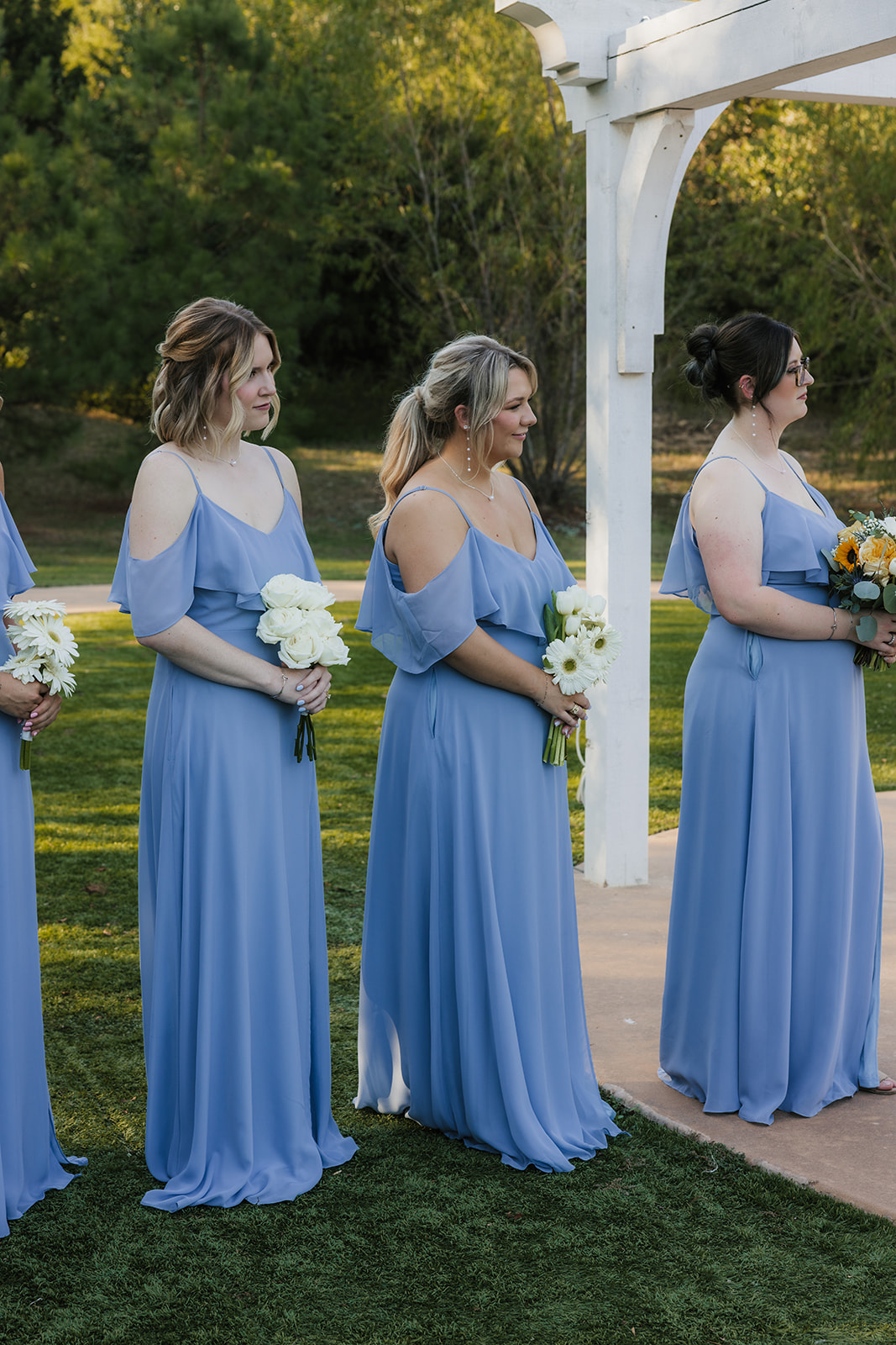 A bride and groom kiss under a white pergola during an outdoor wedding ceremony, with guests and an officiant present at The Silo Event Center in Tulsa