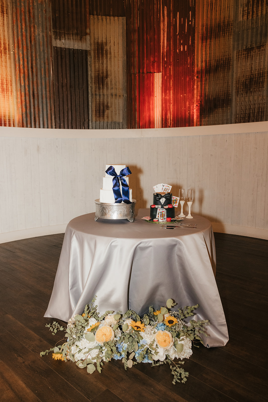 A bride and groom wearing cowboy hats feed each other cake beside a decorated wedding cake and glasses of champagne.
