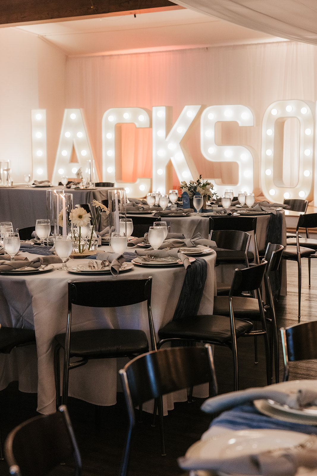 A round table set for a formal event with white plates, silverware, water glasses, cloth napkins, and a flower centerpiece labeled “Table Four.”.