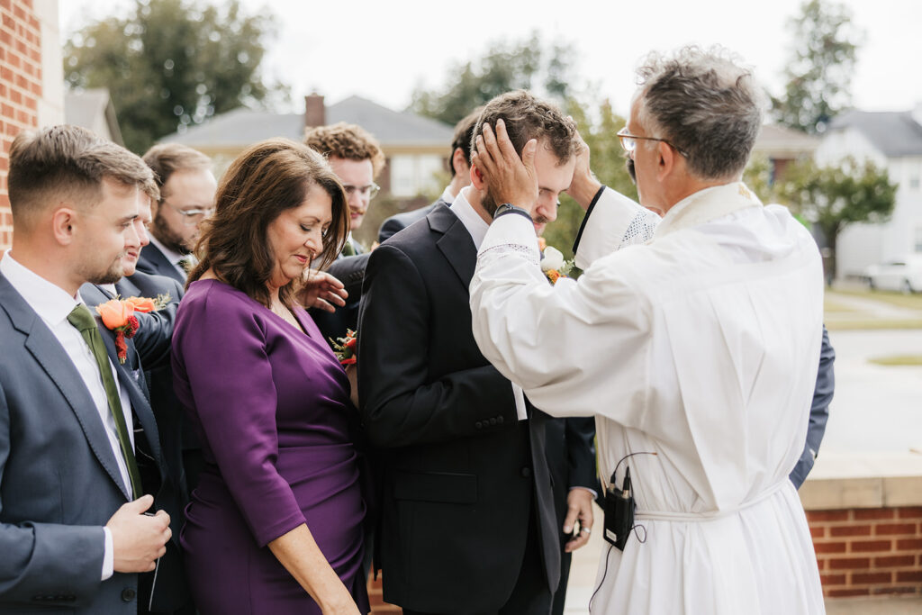 priest praying over the groom before his wedding ceremony